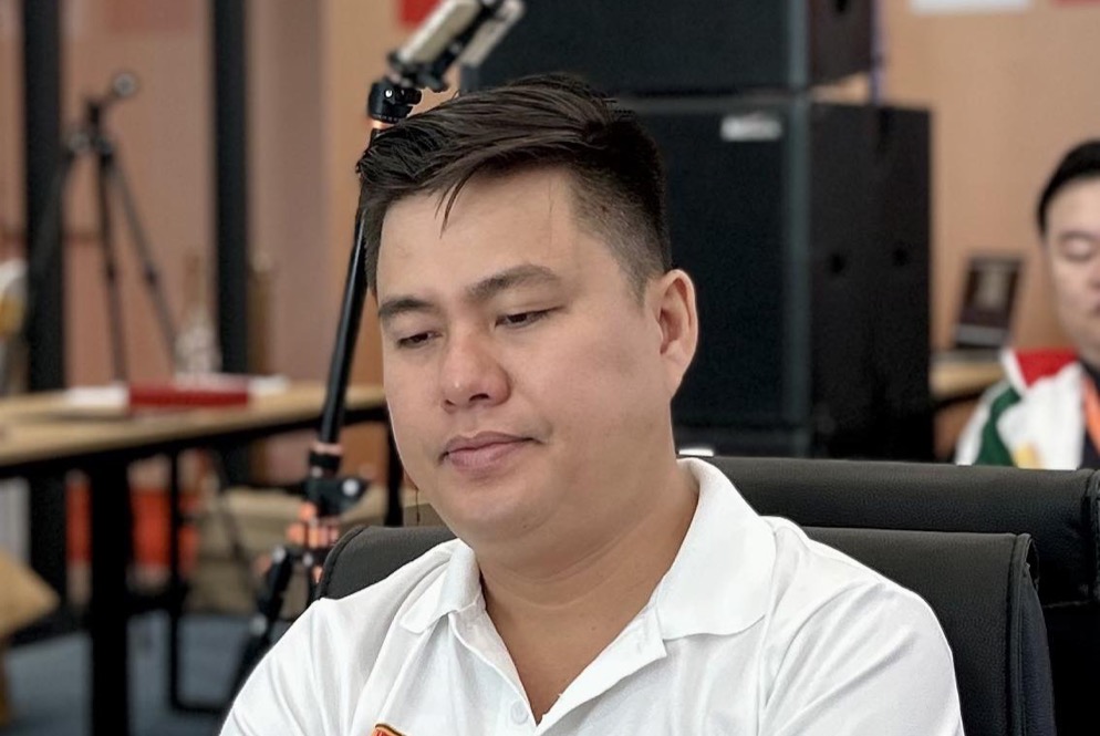 Lại Lý Huynh in a white team shirt, arms folded, looking down at the board during a game.